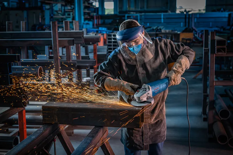 Una persona que usa equipo de seguridad muele metal, creando chispas en un taller industrial.