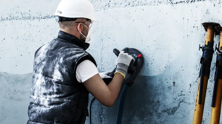 Una persona que usa equipo de seguridad pule una pared de hormigón con una herramienta eléctrica.