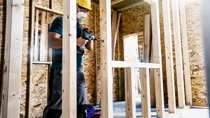 Una persona que usa equipo de seguridad perfora un marco de madera en un sitio de construcción.