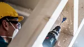 Una persona que usa equipo de seguridad perfora un agujero en vigas de madera.