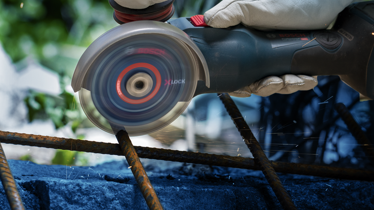 Una persona que usa equipo de seguridad utiliza una amoladora angular para cortar barras de refuerzo oxidadas.