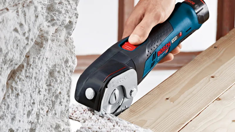 Una persona corta material aislante con una cizalla universal inalámbrica al lado de tablas de madera.