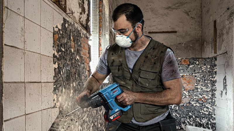 Una persona que usa equipo de seguridad quita azulejos de una pared usando una herramienta eléctrica.