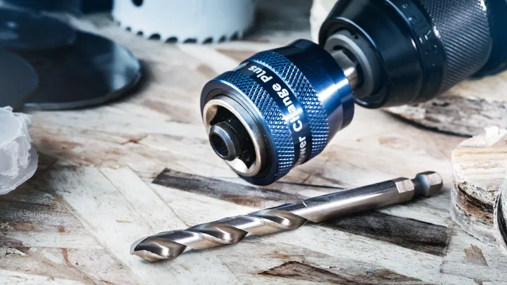 Primer plano de un accesorio de portabrocas con una broca de metal sobre una superficie de madera.