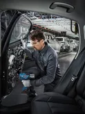 Una persona que usa equipo de seguridad utiliza una herramienta eléctrica para ensamblar la puerta de un automóvil en una fábrica de automóviles.