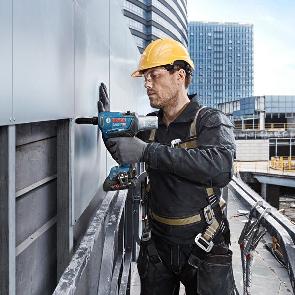 Una persona que usa equipo de seguridad utiliza un taladro eléctrico para fijar paneles en el exterior de un edificio.