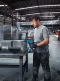 Una persona que usa equipo de seguridad asegura conductos de metal utilizando una pistola remachadora inalámbrica.