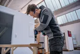 Una persona que usa equipo de seguridad perfora un agujero en la madera usando un taladro eléctrico inalámbrico.
