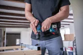 Una persona perfora una viga de metal usando un destornillador inalámbrico dentro de un taller.