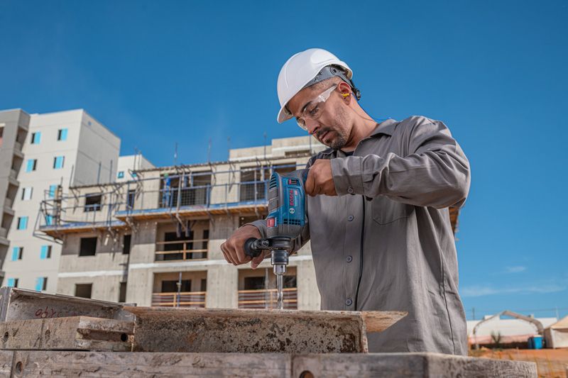 Una persona que usa equipo de seguridad utiliza un taladro de impacto en un sitio de construcción.