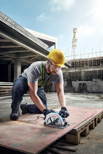 Una persona que usa equipo de seguridad opera una sierra circular para cortar madera contrachapada en un sitio de construcción.