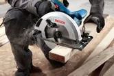 Una persona que usa equipo de seguridad utiliza una sierra circular para cortar una tabla de madera.