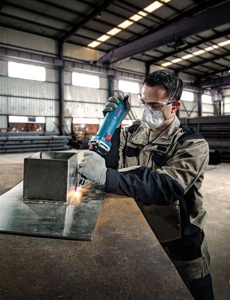 Una persona que usa equipo de seguridad utiliza una amoladora recta sobre una lámina de metal.