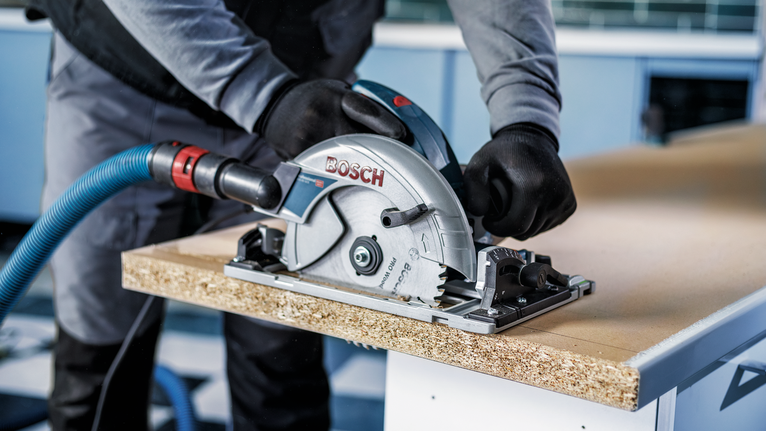 Persona que usa equipo de seguridad corta un panel de madera con una sierra circular.