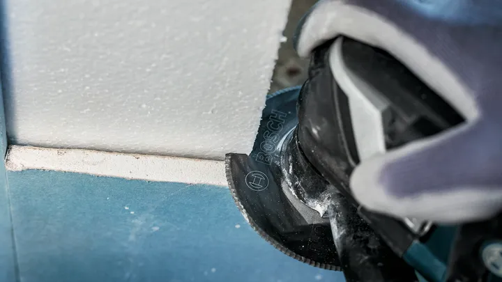 Persona que usa equipo de seguridad corta placas de yeso con una herramienta eléctrica.