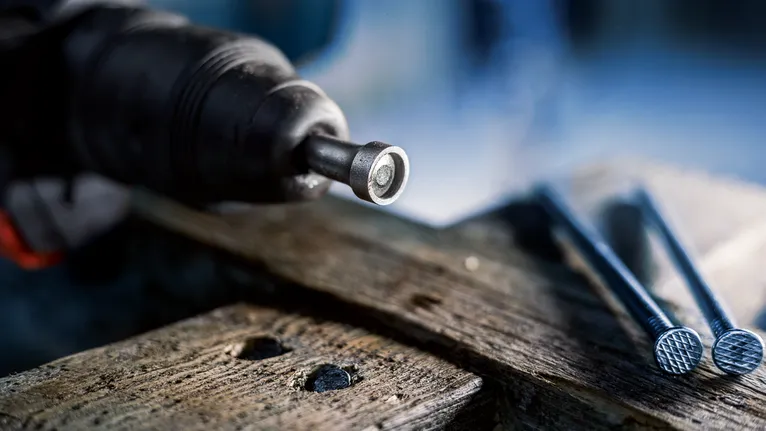 Herramienta eléctrica que coloca un sujetador en la madera junto a varios clavos grandes.