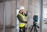 Una persona que lleva equipo de seguridad alinea un montante metálico utilizando una herramienta de nivelación láser.