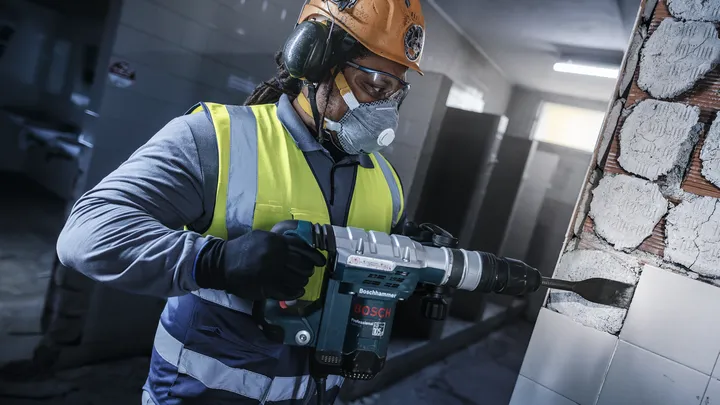 Una persona que usa equipo de seguridad utiliza un martillo rotatorio para quitar azulejos de una pared.