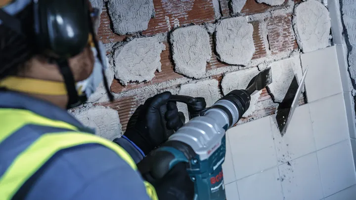 Una persona que usa equipo de seguridad utiliza una herramienta eléctrica para quitar azulejos de una pared.
