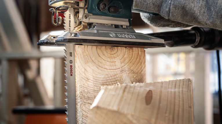 Una persona que usa equipo de seguridad utiliza una sierra caladora para cortar una viga de madera.