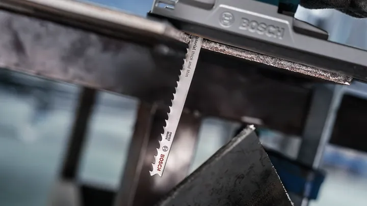 Una persona que usa equipo de seguridad utiliza una sierra caladora para cortar una lámina de metal.