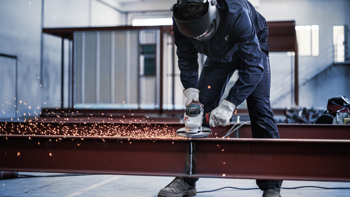 Una persona que usa equipo de seguridad muele una viga de metal, produciendo chispas.