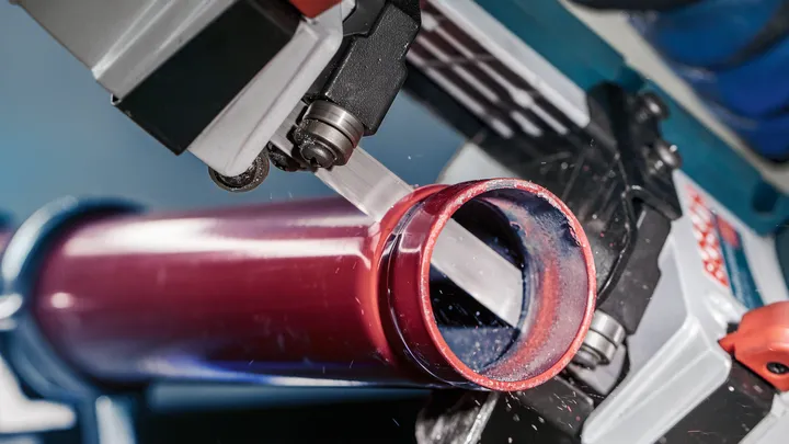 Una sierra de cinta corta un tubo de metal rojo en un taller.