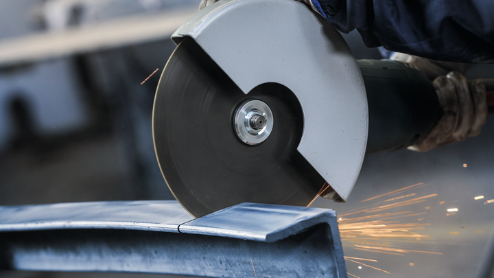 Persona que usa equipo de seguridad corta metal con una sierra circular, produciendo chispas.