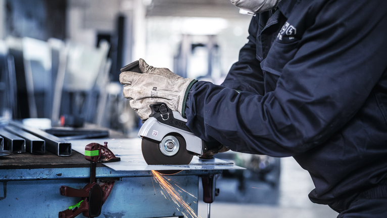 Una persona que usa equipo de seguridad utiliza una amoladora angular para cortar metal, produciendo chispas.