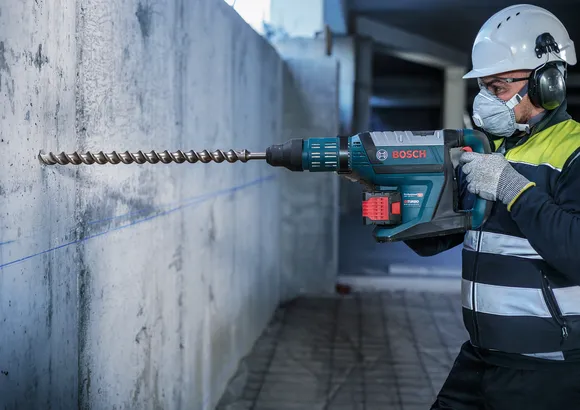 Una persona que usa equipo de seguridad perfora una pared de hormigón con un martillo perforador.
