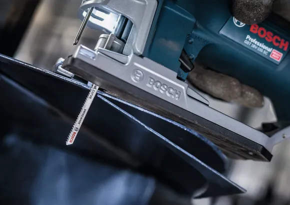 Una persona que usa equipo de seguridad utiliza una sierra de calar para cortar una lámina de metal.