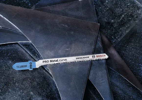 Una hoja de sierra caladora de metal reposa sobre piezas de chapa metálica apiladas.