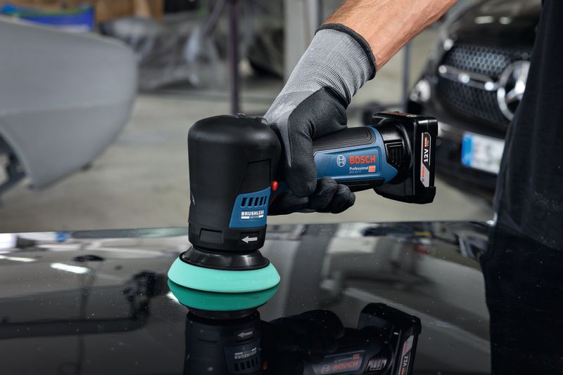 Una persona que usa equipo de seguridad utiliza una pulidora inalámbrica en la superficie de un automóvil.