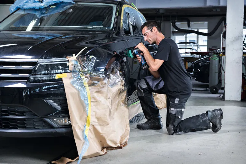 Una persona que usa equipo de seguridad pule el guardabarros de un automóvil en un taller.