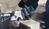 Una persona que usa equipo de seguridad corta un bloque de hormigón con una sierra amoladora inalámbrica.