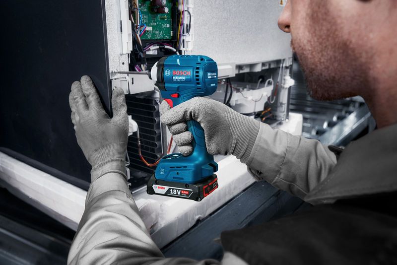 Una persona que usa equipo de seguridad utiliza un destornillador de impacto inalámbrico para ensamblar componentes electrónicos.