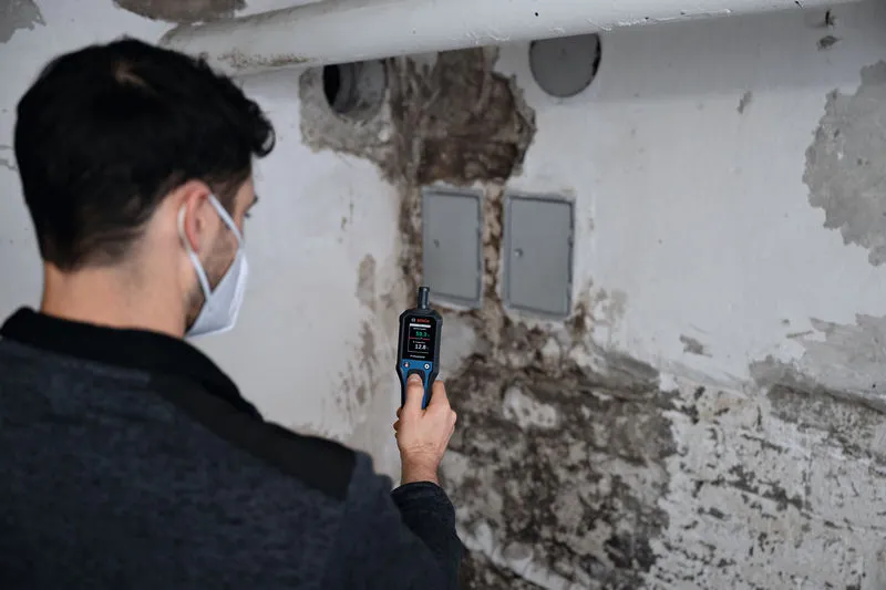 Una persona que usa equipo de seguridad comprueba la humedad de la pared utilizando un termohigrómetro.