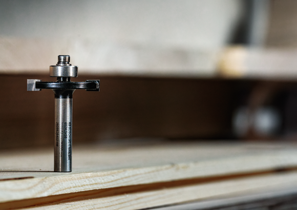 Broca de enrutador colocada en posición vertical sobre tablas de madera apiladas en el interior.