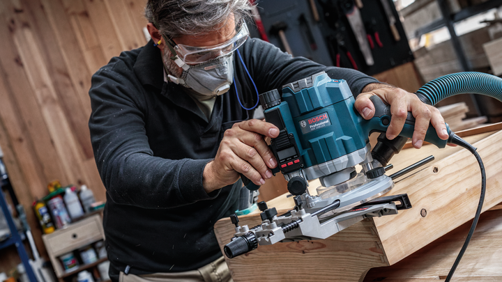 Una persona que usa equipo de seguridad opera una herramienta eléctrica para dar forma a la madera en un taller.