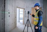 Una persona que usa equipo de seguridad utiliza una herramienta niveladora láser para proyectar líneas verdes en una pared de concreto.