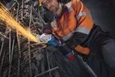 Un trabajador que usa equipo de seguridad utiliza una amoladora angular para cortar barras de refuerzo de metal.