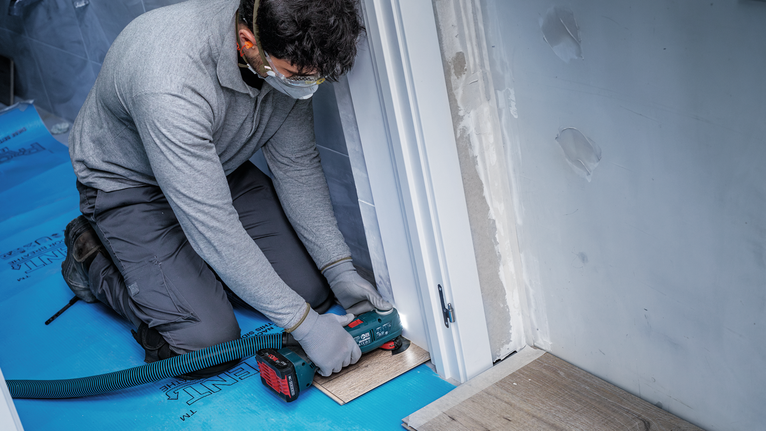 Una persona que usa equipo de seguridad usa una herramienta eléctrica para cortar el piso cerca de una puerta.