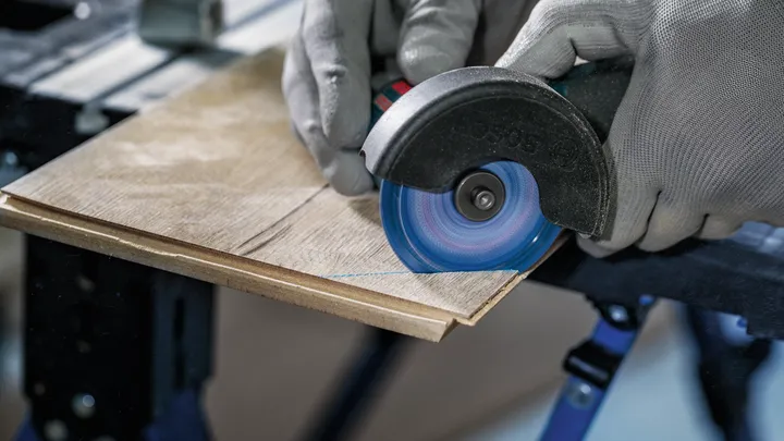 Una persona que usa equipo de seguridad corta una tabla de madera con una amoladora angular.