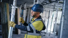 Una persona que lleva equipo de seguridad utiliza un martillo para ajustar un andamio en una obra de construcción.