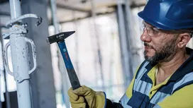 Una persona que lleva equipo de seguridad utiliza un martillo en un poste de metal en una obra de construcción.