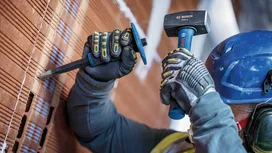 Una persona que lleva equipo de seguridad utiliza un martillo y un cincel en una pared de ladrillos.