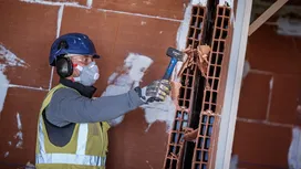 Una persona que lleva equipo de seguridad utiliza un martillo para romper un muro de bloques de arcilla.
