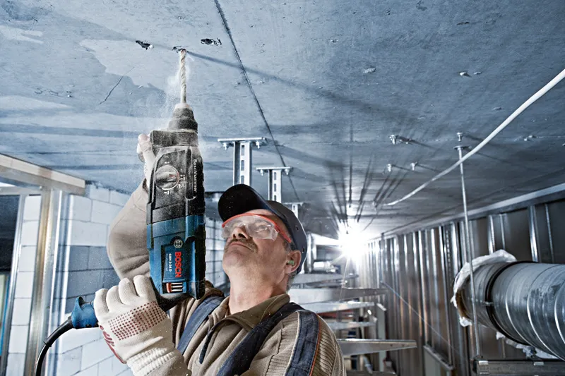 Una persona que usa equipo de seguridad perfora un techo de hormigón en un entorno industrial.