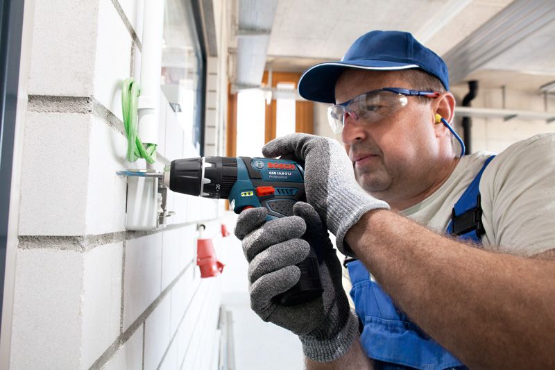 Eine Person mit Schutzausrüstung verwendet einen Akku-Schlagbohrschrauber an einer Wand.