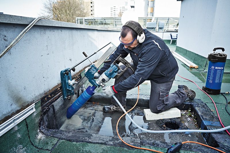 Eine Person mit Sicherheitsausrüstung bohrt mit einem montierten Diamantbohrer in Beton.